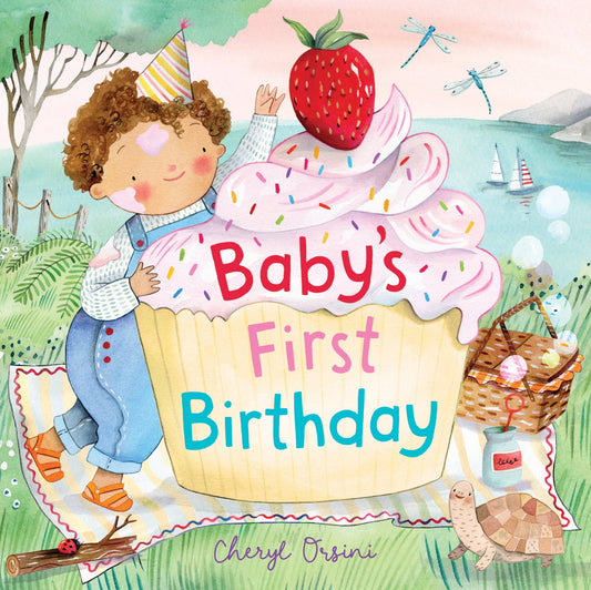 Illustrated children's book cover titled "Baby's First Birthday" by Cheryl Orsini, showing a baby peeking from behind a giant strawberry cupcake on a picnic blanket by the water.
